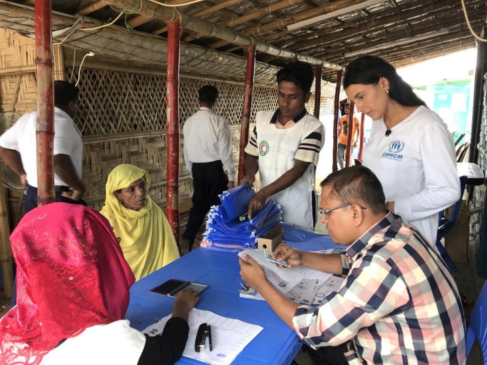 Two Rohingya women in head scarves sit at a table getting identification documents from a man sitting across from them