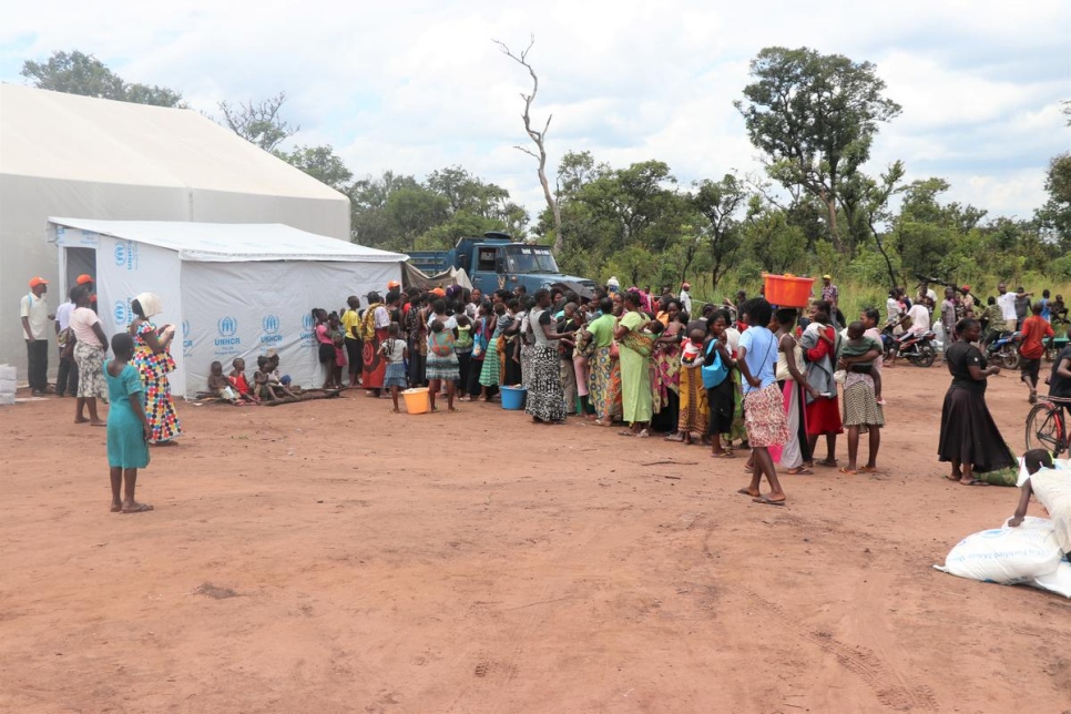 A group of Congolese people from DRC stand beside a shed with UNHCR branding