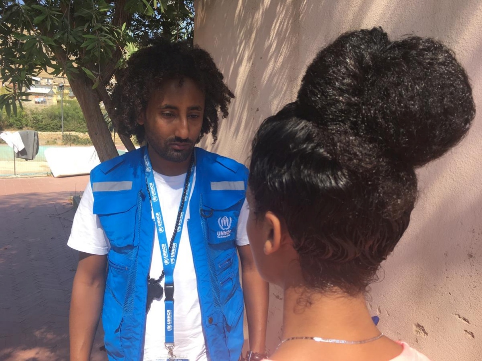 Woman speaks to a a man wearing UNHCR branded blue vest