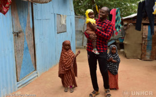 A Somali man stands outside of his home with his three young daughters