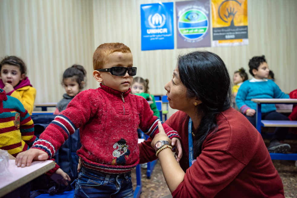 Humanitarian aid worker helps guide a visually impaired child around a classroom