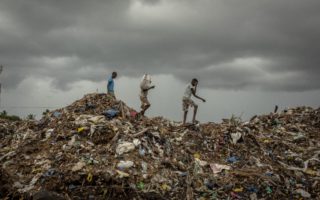 Three young men traversing a top a mountain of garbage