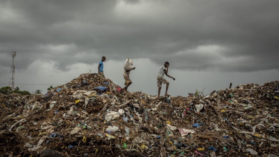 Three young men traversing a top a mountain of garbage