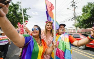 Three people in El Salvador holding rainbow flags and taking selfies