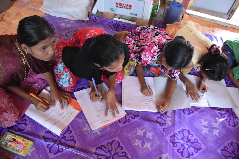 Four Rohingya girls kneel on the floor as they work on their school assignment