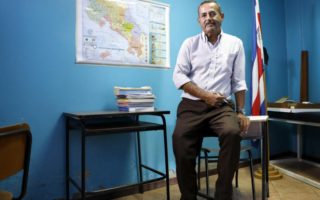 A Nicaraguan professor sits on a desk in a blue room