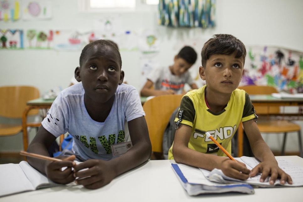 Two refugee children sit side by side doing their schoolwork and gaining an education