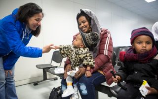 A woman says hi to a baby who is sitting on his mother's lap at a facility welcoming arrivals from Libya