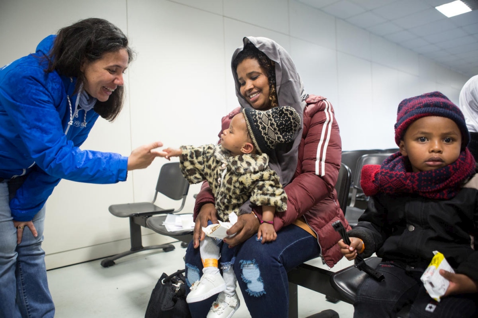 A woman says hi to a baby who is sitting on his mother's lap at a facility welcoming arrivals from Libya