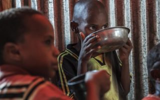 Two young children drink eat in a shelter in Ethiopia