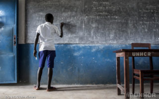 Young boy from South Sudan writes on a chalkboard as he pursues his education