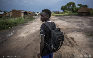 Young refugee boy from South Sudan walks down a dirt road with backpack to go to school and pursue his education