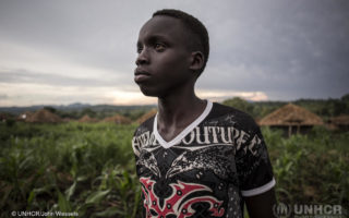 Young boy from South Sudan who is pursuing his education looks off to the distance as he stands in an outdoor field