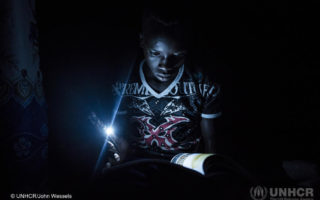 Young boy from South Sudan studies by solar lamp as he pursues his education
