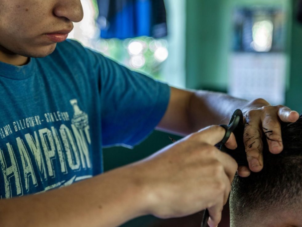 Man cuts another man's hair in San Salvador