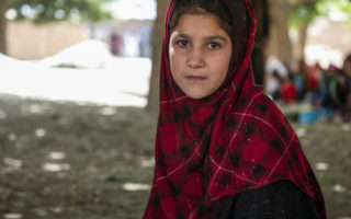 An Afghan girl sits under a tree