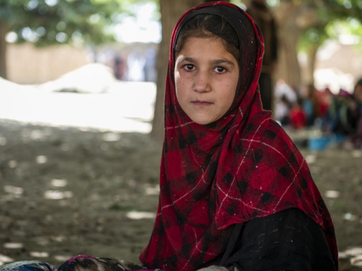 An Afghan girl receiving an education sits under a tree
