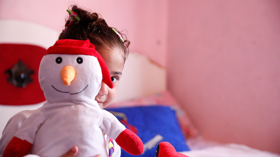 A young refugee child in Mexico obscures her face behind a stuffed snowman