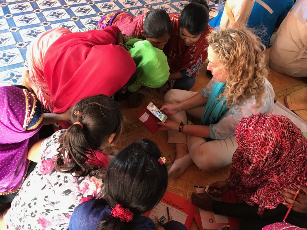 UNHCR staffer shows group of Rohingya girls something on her smart phone