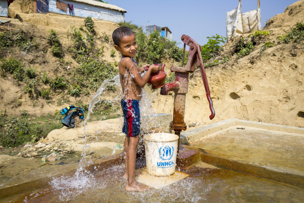 A Rohingya boy fills a bucket and kettle at a water pump