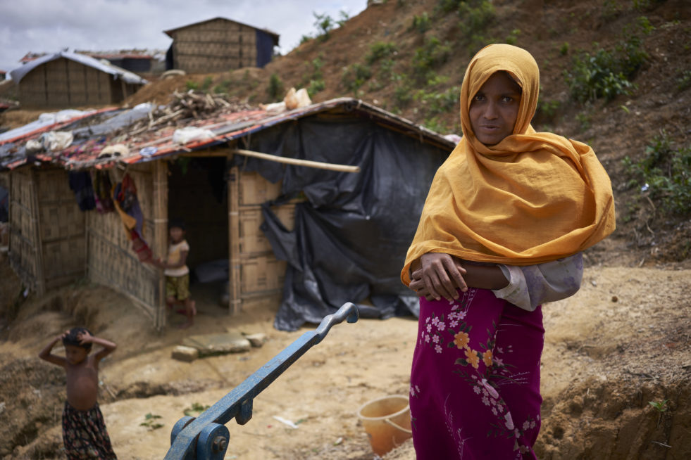 A Rohingya poses for a photograph outside of her home by a water pump