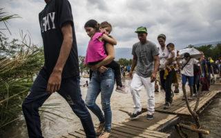 A group of Venezuelans cross a river over a rickety make-shift bridge