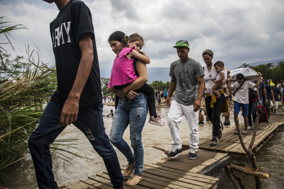 A group of Venezuelans cross a river over a rickety make-shift bridge