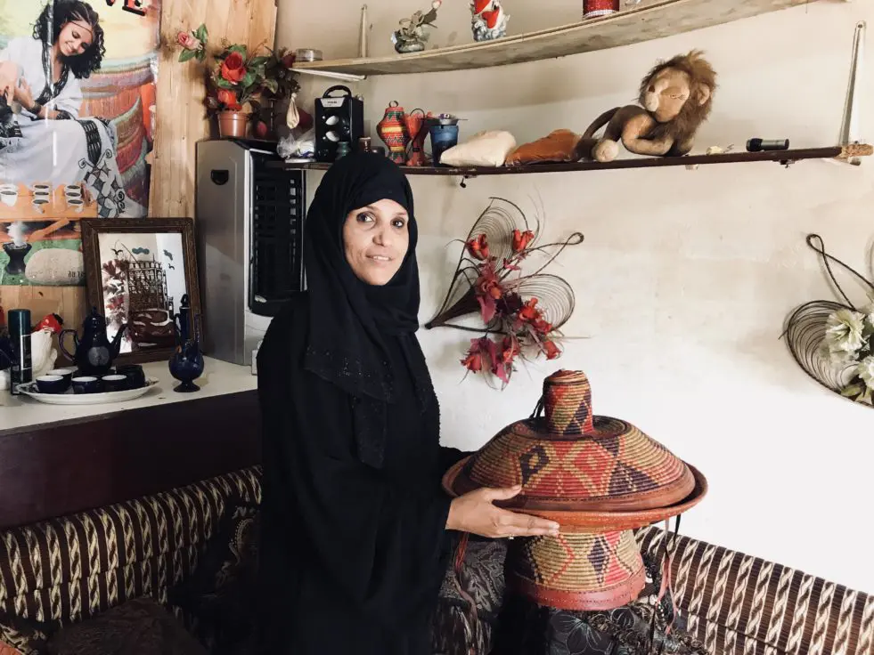 Woman from Yemen holds a woven piece of furniture