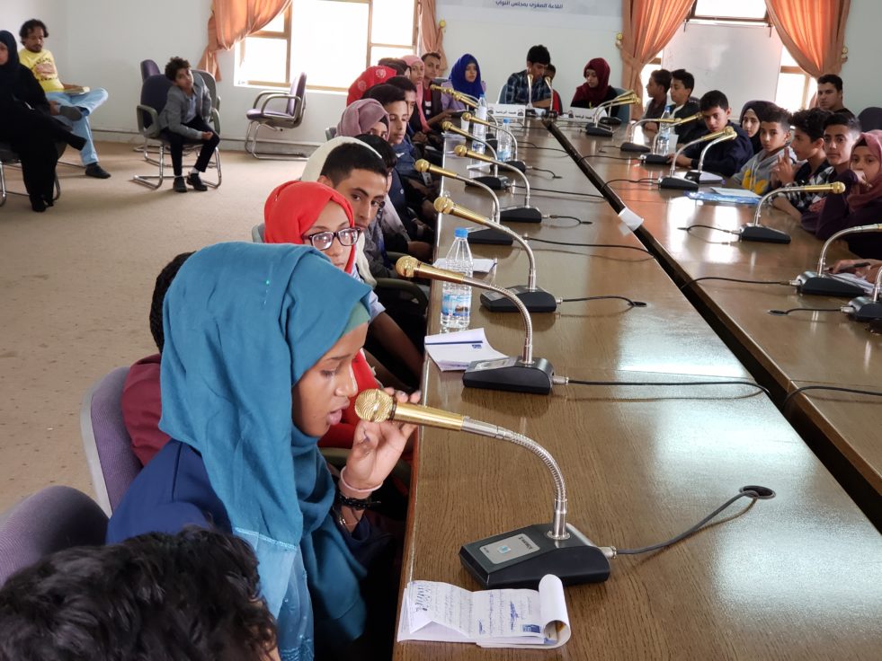 Children sits at a table speaking into microphones in Yemen
