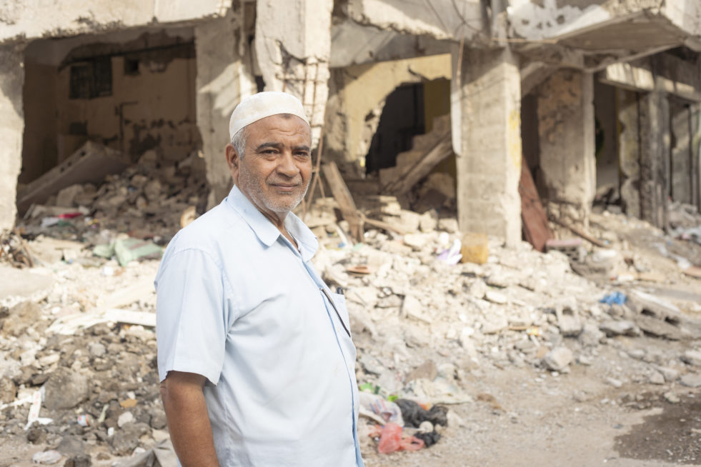 Older man standing in front of the ruins of a building in Yemen