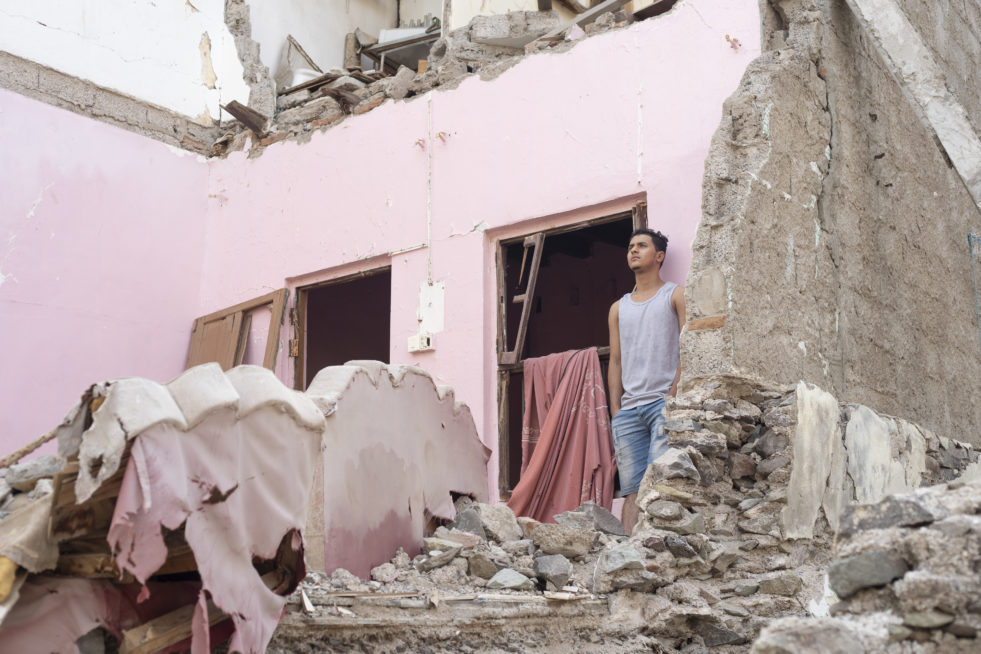 A young man stands in the ruins of his old home in Yemen