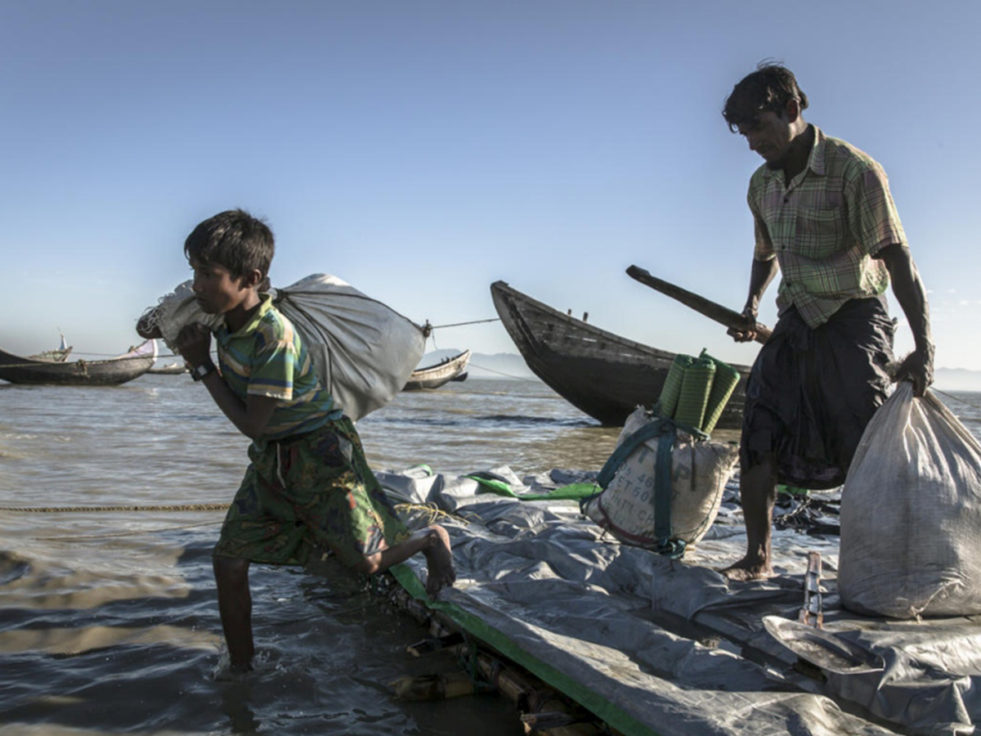 A man and a young boy lift bags off a boat in South East Asia