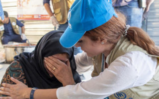A woman from Syria cries beside another woman wearing UNHCR branded clothing.