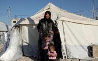 Nadira, une réfugiée syrienne, se tient au soleil devant sa tente familiale dans le camp de Bardarash, gouvernorat de Dohouk, avec son fils de trois ans et sa fille de quatre ans. Leur fuite depuis la Syrie a été très difficile et aujourd’hui Nadira craint l’hiver qui s’annonce