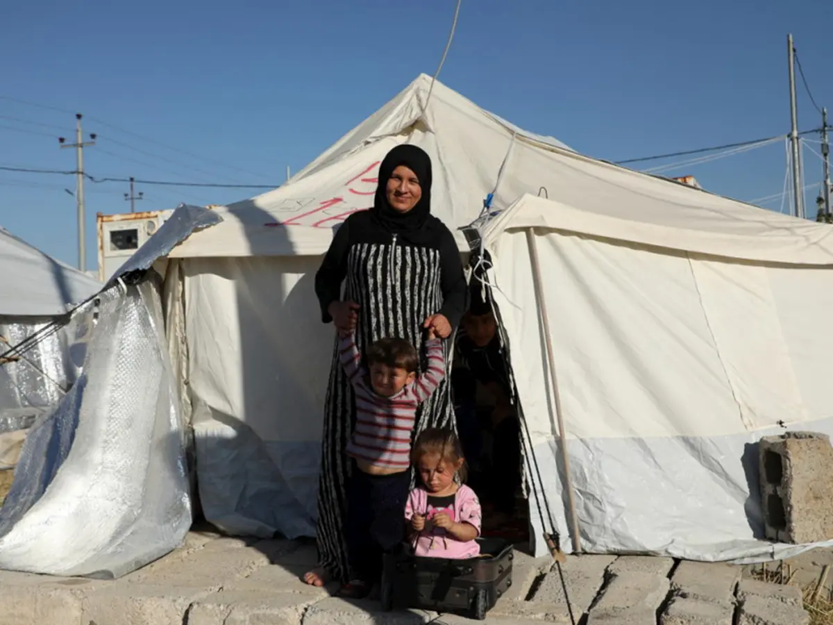 Nadira, une réfugiée syrienne, se tient au soleil devant sa tente familiale dans le camp de Bardarash, gouvernorat de Dohouk, avec son fils de trois ans et sa fille de quatre ans. Leur fuite depuis la Syrie a été très difficile et aujourd’hui Nadira craint l’hiver qui s’annonce