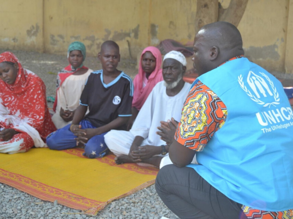 Refugees sit on the ground while talking to a UNHCR staff member about resettlement