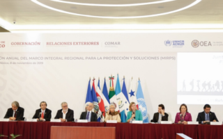 A group of people sit at a table with flags behind them