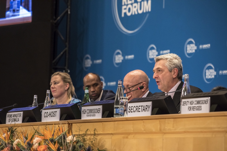 High Commissioner for Refugees sits on a panel at the global refugee forum with a blue backdrop behind him