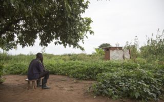 Refugee from South Sudan sits on a stool under a tree in Uganda