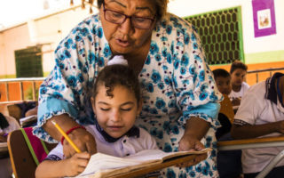 A female teacher helps a young refugee girl with her school work