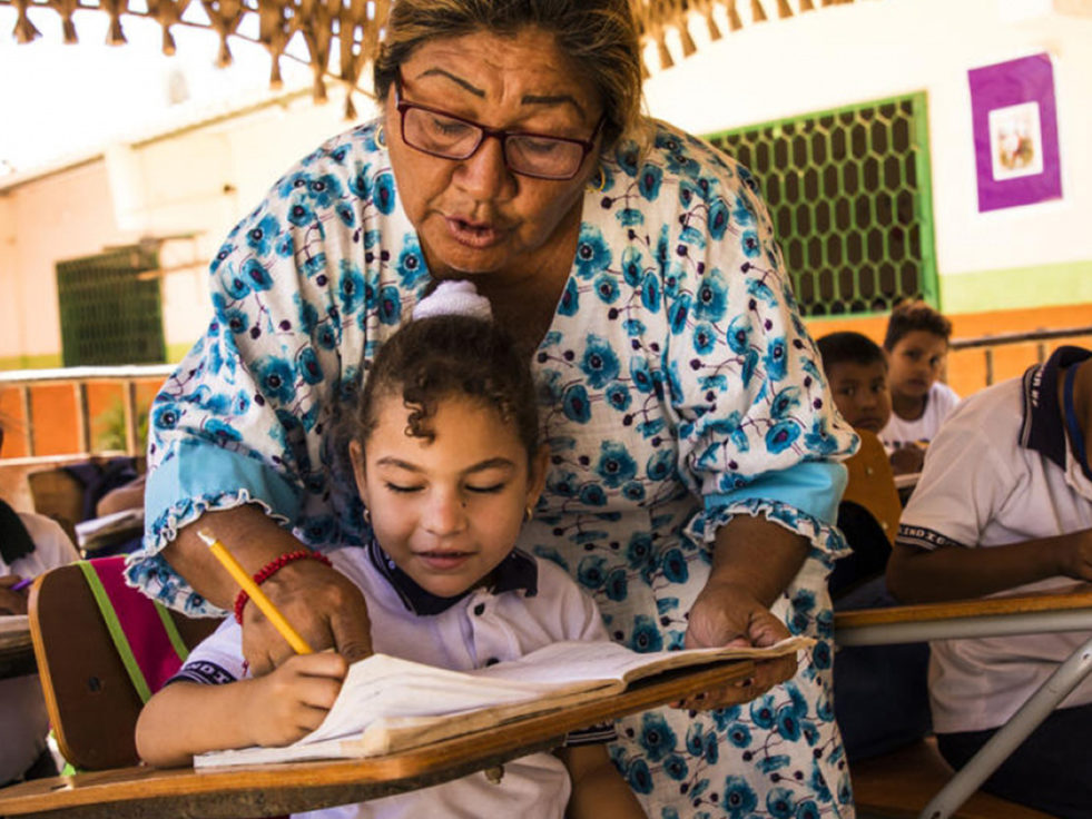 A female teacher helps a young refugee girl with her school work