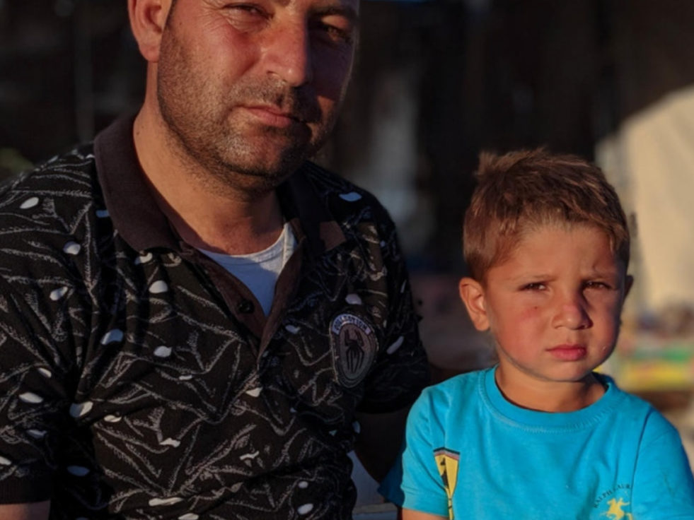 Un réfugié syrien et son fils sont assis dans un camp