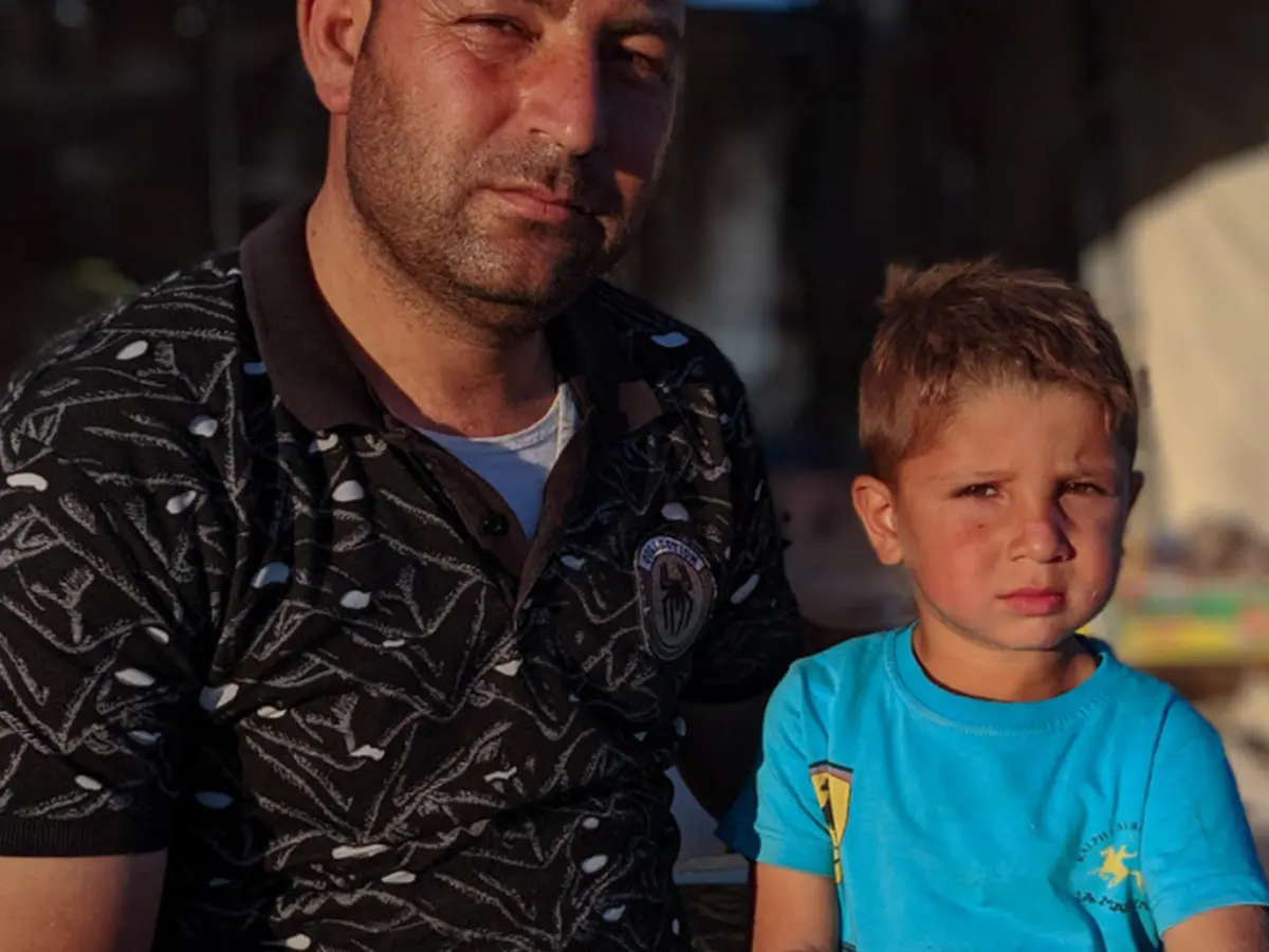 A Syrian refugee and his son sits in a camp