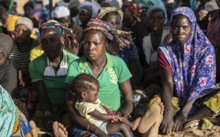 A group of women sit on the ground with the woman at the centre cradling a sleeping child in Burkina Faso