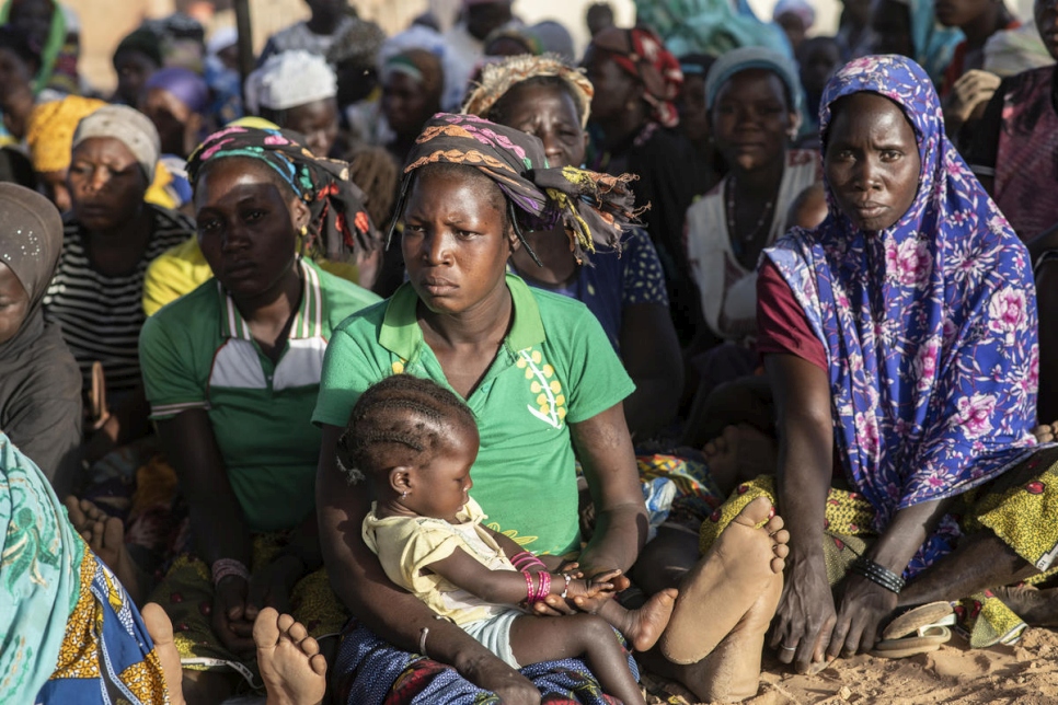 A group of women sit on the ground with the woman at the centre cradling a sleeping child in the Sahel Region