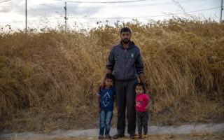 A man stands with his two children in front of a dried bush