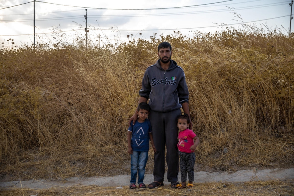 A man stands with his two children in front of a dried bush