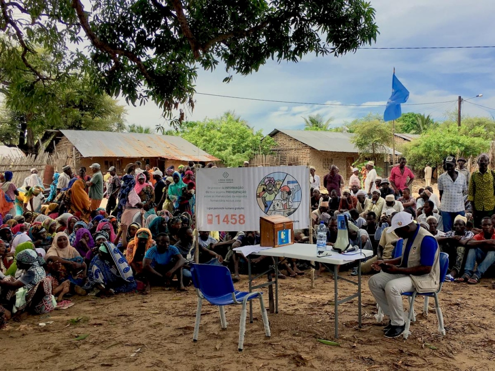 Man sits at a table in front of a sign with a crowd sitting around him in Mozambique