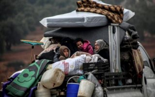 Syrian family sitting in the back of a truck with their belongings.