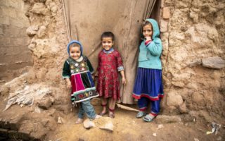 Three Afghan children stand outside of a doorway